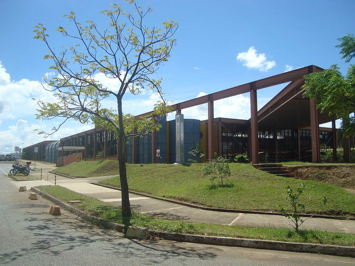 Prédio moderno da Escola de Minas no campus Morro do Cruzeiro da UFOP, com estrutura metálica marrom, fachada de vidro e gramado sob céu azul