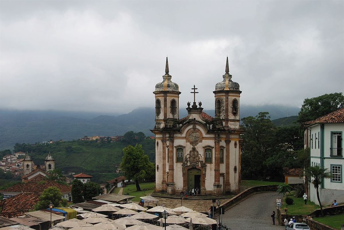Centro Histórico de Ouro Preto com a Igreja de São Francisco de Assis ao centro, barracas da feira de artesanato do Largo de Coimbra em primeiro plano e serras ao fundo