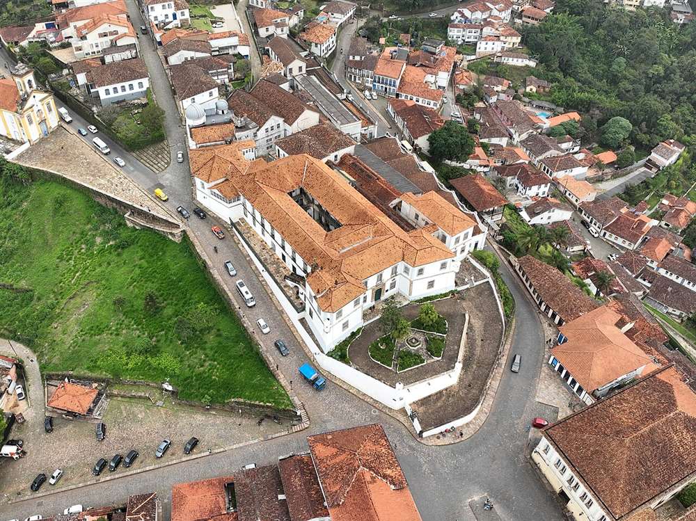 Vista aérea do Palácio dos Governadores em Ouro Preto, prédio branco colonial com muralhas e jardim interno, cercado pelo casario de telhados coloniais do Centro Histórico