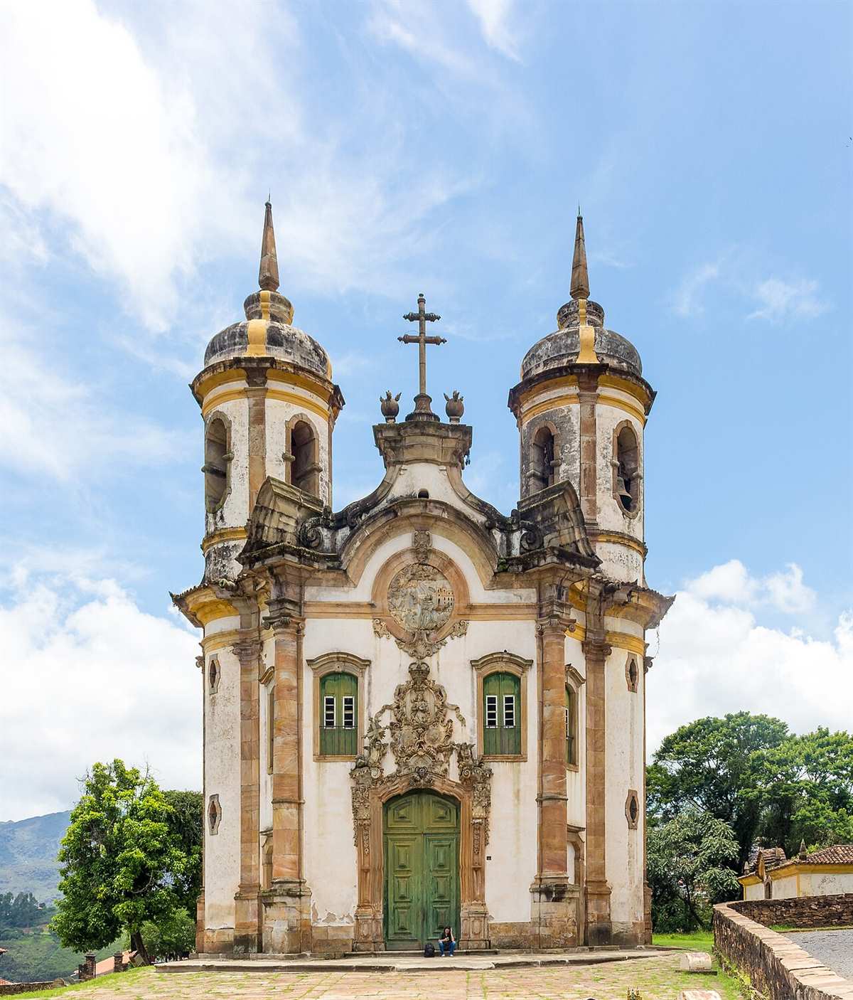 Fachada da Igreja de São Francisco de Assis em Ouro Preto, com duas torres cilíndricas, portada esculpida em pedra-sabão e céu azul com nuvens