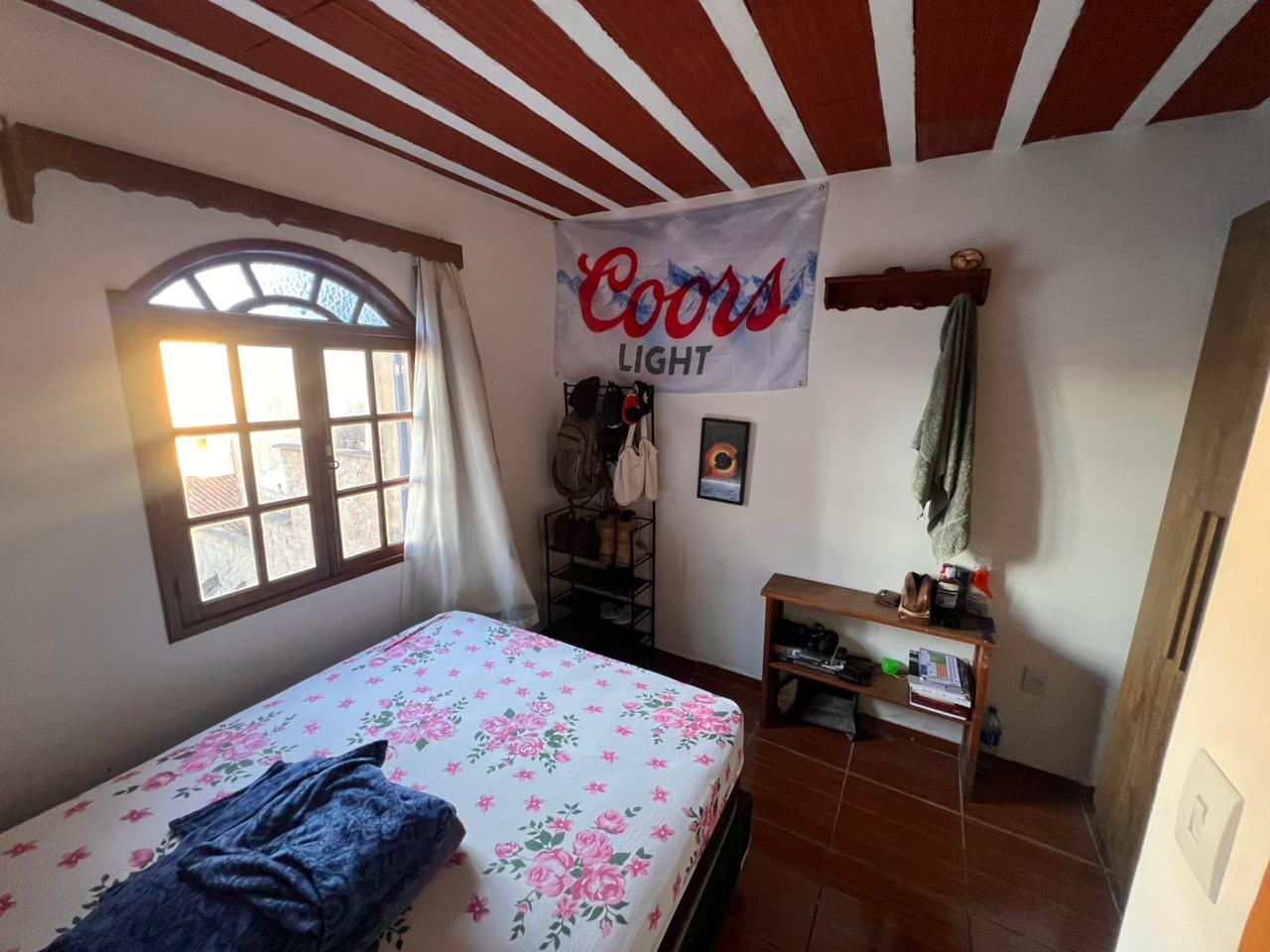 Quarto com cama de casal, teto em madeira vermelho e branco e janela com vista para Ouro Preto